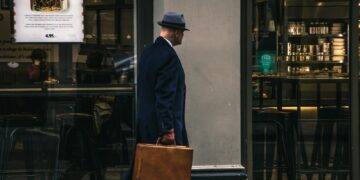 man in black suit jacket and blue hat standing in front of store