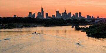 A boat traveling down a river with a city skyline in the background