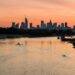 A boat traveling down a river with a city skyline in the background