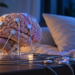 Anatomical brain model with EEG-style leads beside a pillow in blue night lighting, illustrating sleep-based neurological stimulation