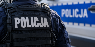 Close-up of a Polish police officer in tactical uniform beside a police vehicle
