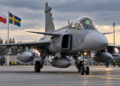 Swedish JAS 39 Gripen fighter aircraft on an airbase apron with Polish and Swedish flags