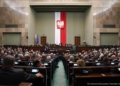 Archive photograph of the Sejm parliamentary chamber in Warsaw, with MPs seated beneath the Polish national emblem.