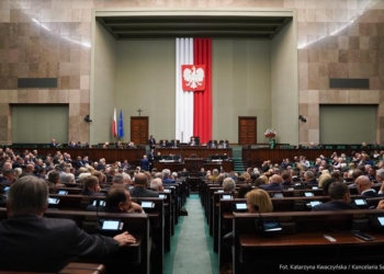 Archive photograph of the Sejm parliamentary chamber in Warsaw, with MPs seated beneath the Polish national emblem.