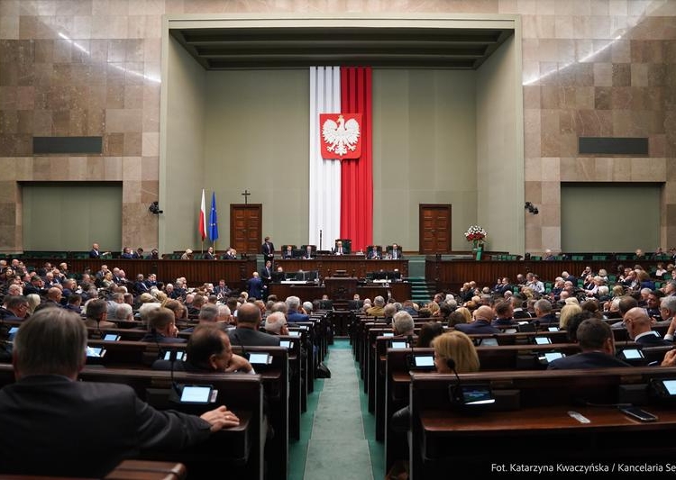 Archive photograph of the Sejm parliamentary chamber in Warsaw, with MPs seated beneath the Polish national emblem.