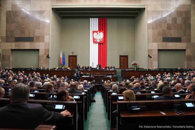 Archive photograph of the Sejm parliamentary chamber in Warsaw, with MPs seated beneath the Polish national emblem.