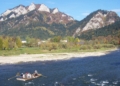 Traditional Dunajec raftsmen with passengers on a wooden raft travelling beneath the limestone peaks of Trzy Korony and Facimiech in the Pieniny Mountains, October 2006