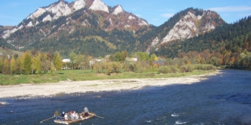 Traditional Dunajec raftsmen with passengers on a wooden raft travelling beneath the limestone peaks of Trzy Korony and Facimiech in the Pieniny Mountains, October 2006