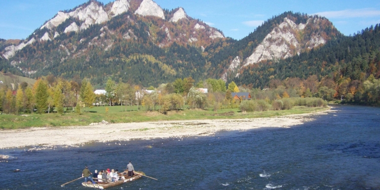 Traditional Dunajec raftsmen with passengers on a wooden raft travelling beneath the limestone peaks of Trzy Korony and Facimiech in the Pieniny Mountains, October 2006