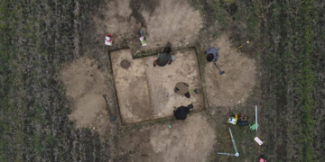 Overhead photograph of four archaeological researchers examining an excavation trench in a field at Gródek, eastern Poland. Image from the Stanisław Staszic Museum in Hrubieszów.