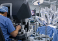 Digital illustration of a surgeon using a robotic surgical console while covered robotic arms stand in a modern operating theatre.