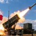 Digital editorial illustration of a Patriot-style missile launching from a mobile launcher beneath a Polish flag. Symbolic imagery, not an actual event.