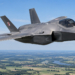 Digitally created illustration of a Polish F-35A Husarz fighter flying above green fields and a river in Poland