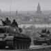 AI-generated editorial illustration of Soviet armoured columns with Warsaw in the background, representing the October 1956 crisis; not an authentic historical photograph