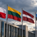 Digitally created illustration of Polish, Lithuanian, Latvian and Estonian flags outside a modern building beneath cloudy skies.