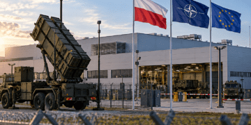 Editorial image of a European defence factory under air-defence protection with Polish, NATO and EU flags