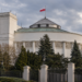 Digitally created architectural illustration of the Polish Sejm parliament building in Warsaw beneath an overcast sky, with the Polish flag flying