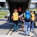 People accompanied by officers walking towards the open rear ramp of a military transport aircraft.
