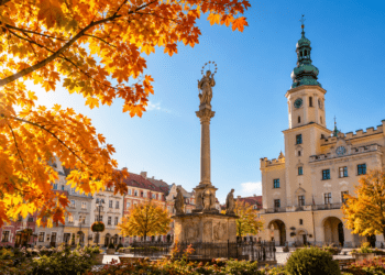Digitally generated editorial illustration of golden autumn trees and a sunny historic Polish town square, representing unusually mild October weather.