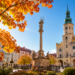 Digitally generated editorial illustration of golden autumn trees and a sunny historic Polish town square, representing unusually mild October weather.