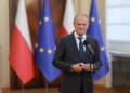 A government official at a microphone with Polish and European Union flags in the background