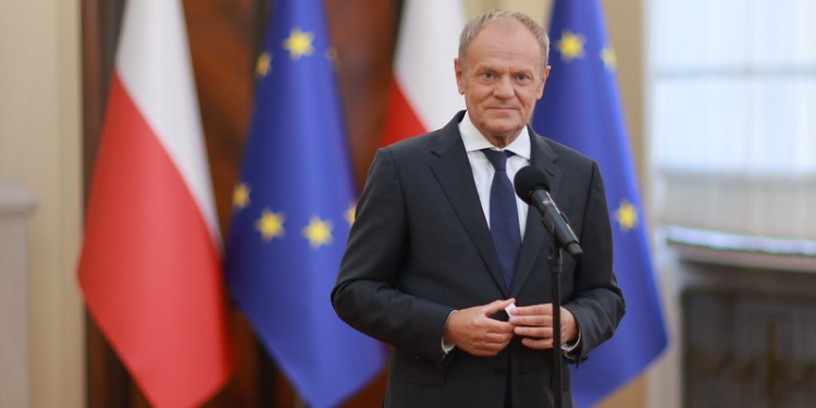 A government official at a microphone with Polish and European Union flags in the background