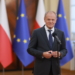 A government official at a microphone with Polish and European Union flags in the background