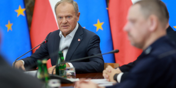 Government officials seated at a conference table with Polish and European Union flags in the background